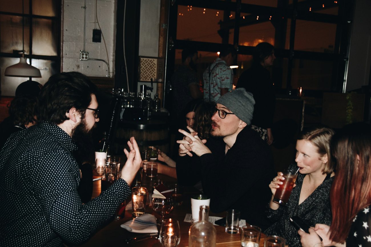 A group around a table in a dark bar, mid-conversation, drinks and candles between them