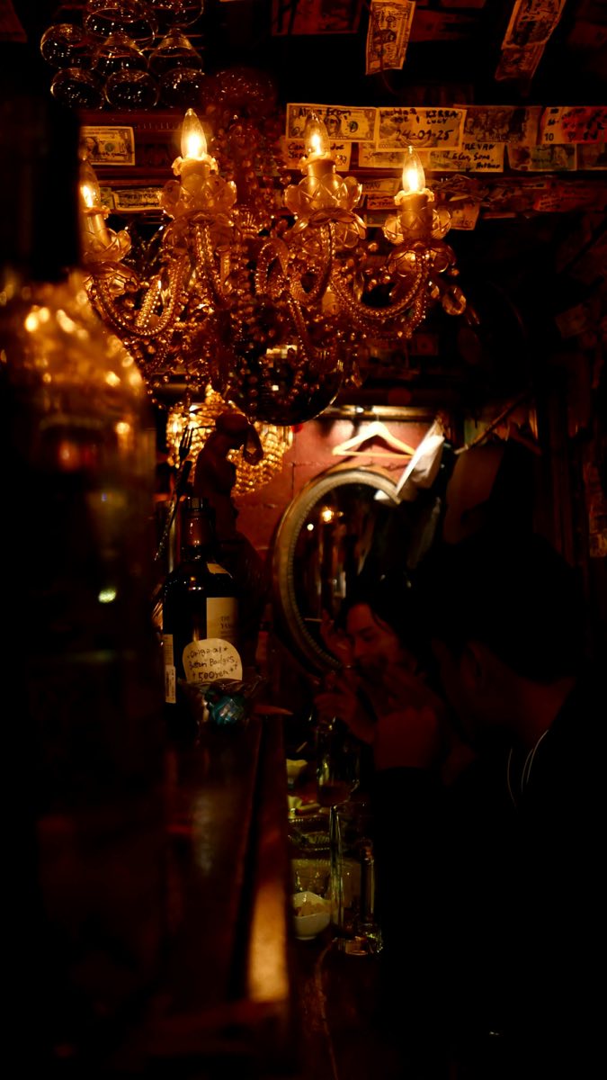 A chandelier lighting a dark old bar, bottles and glasses in deep shadow