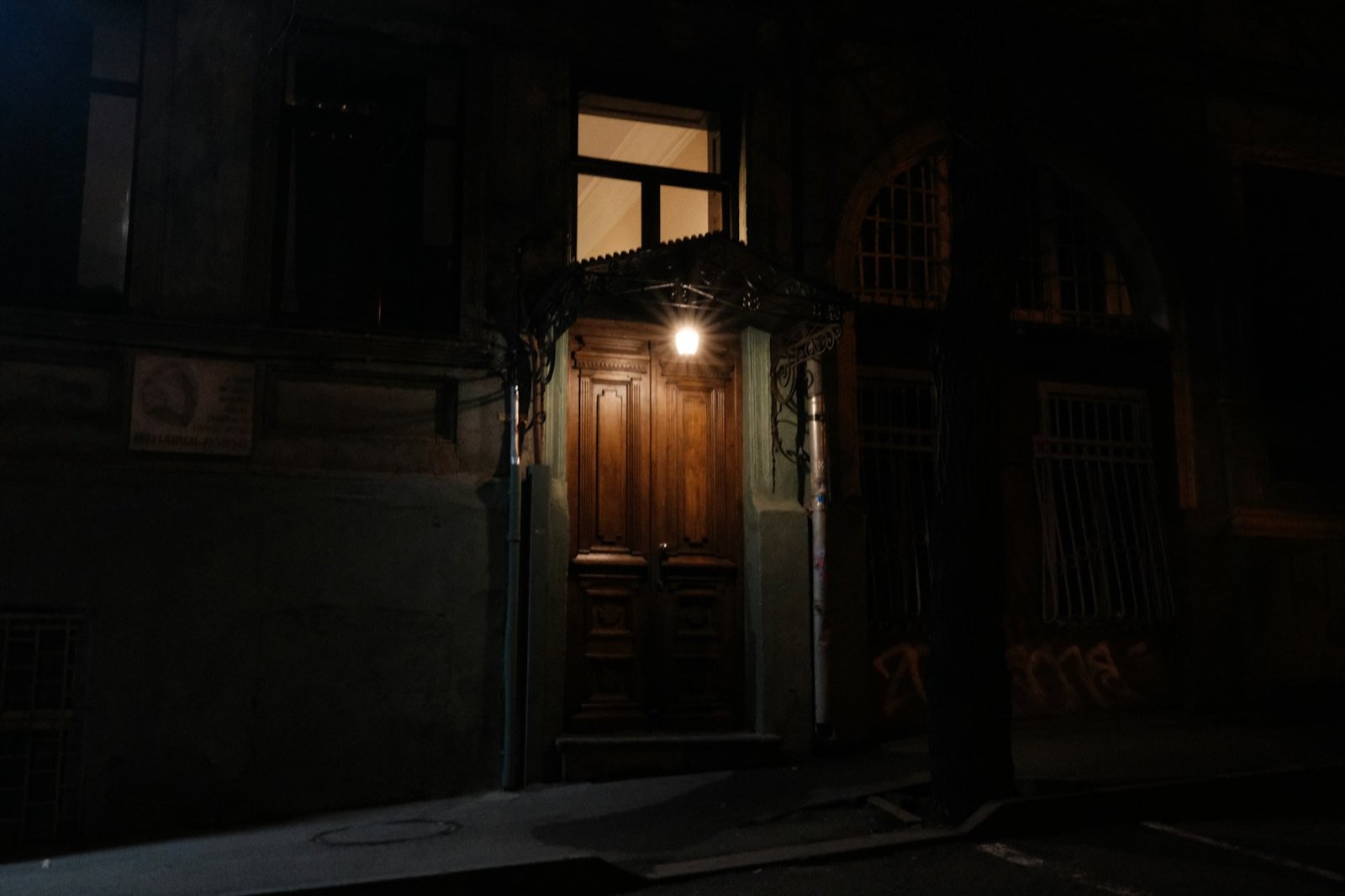An unmarked wooden door on a dark street, lit by a single lamp