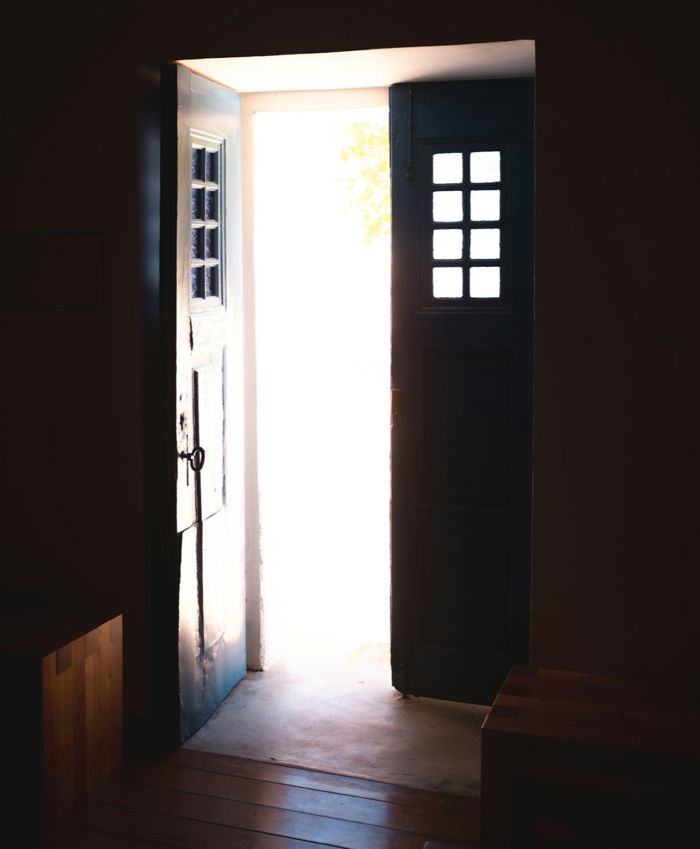 An open door in a dark interior with daylight spilling across the threshold