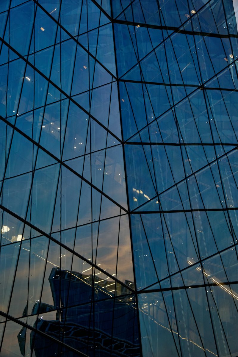 A faceted glass facade reflecting a neighbouring tower at dusk