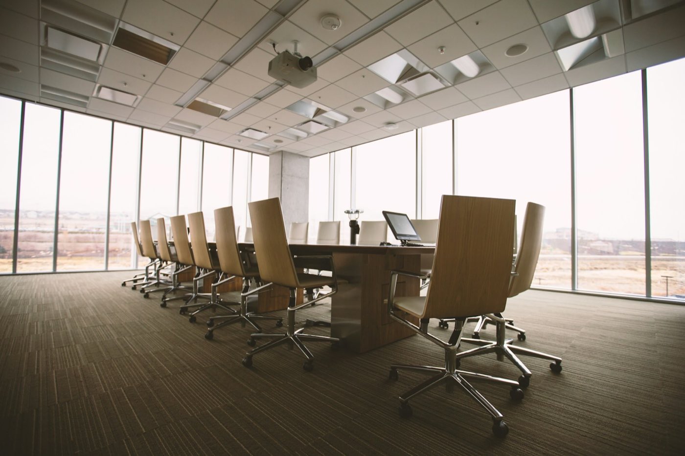 An empty boardroom of high-backed chairs along a long table, windows on both sides
