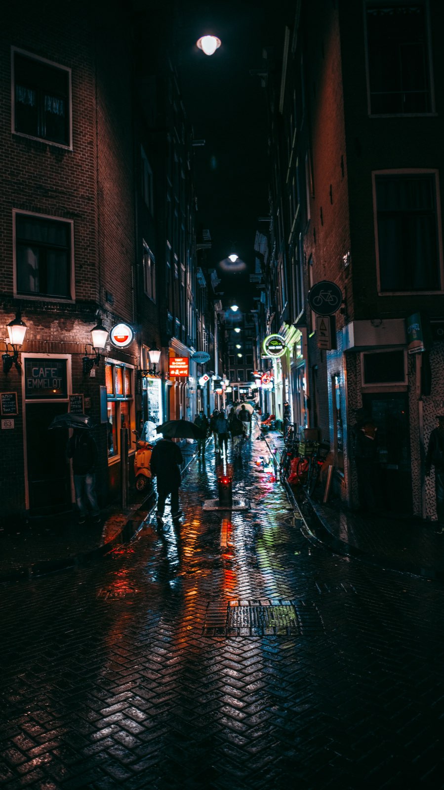 A narrow Amsterdam side street after rain at night, lamplight reflected on wet cobbles