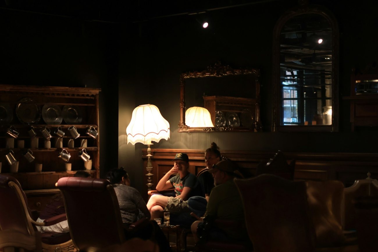 People sitting and talking in a dimly lit vintage lounge, lamplight and old mirrors